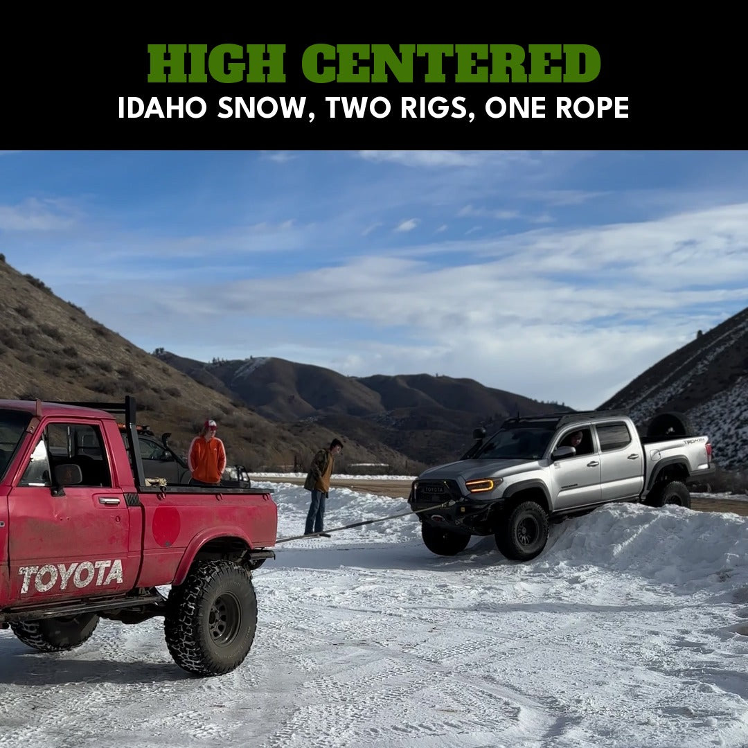 Idaho snow: a Tacoma high-centered on a berm, a red vintage Toyota pulling it on a taut Kinetic-X kinetic rope