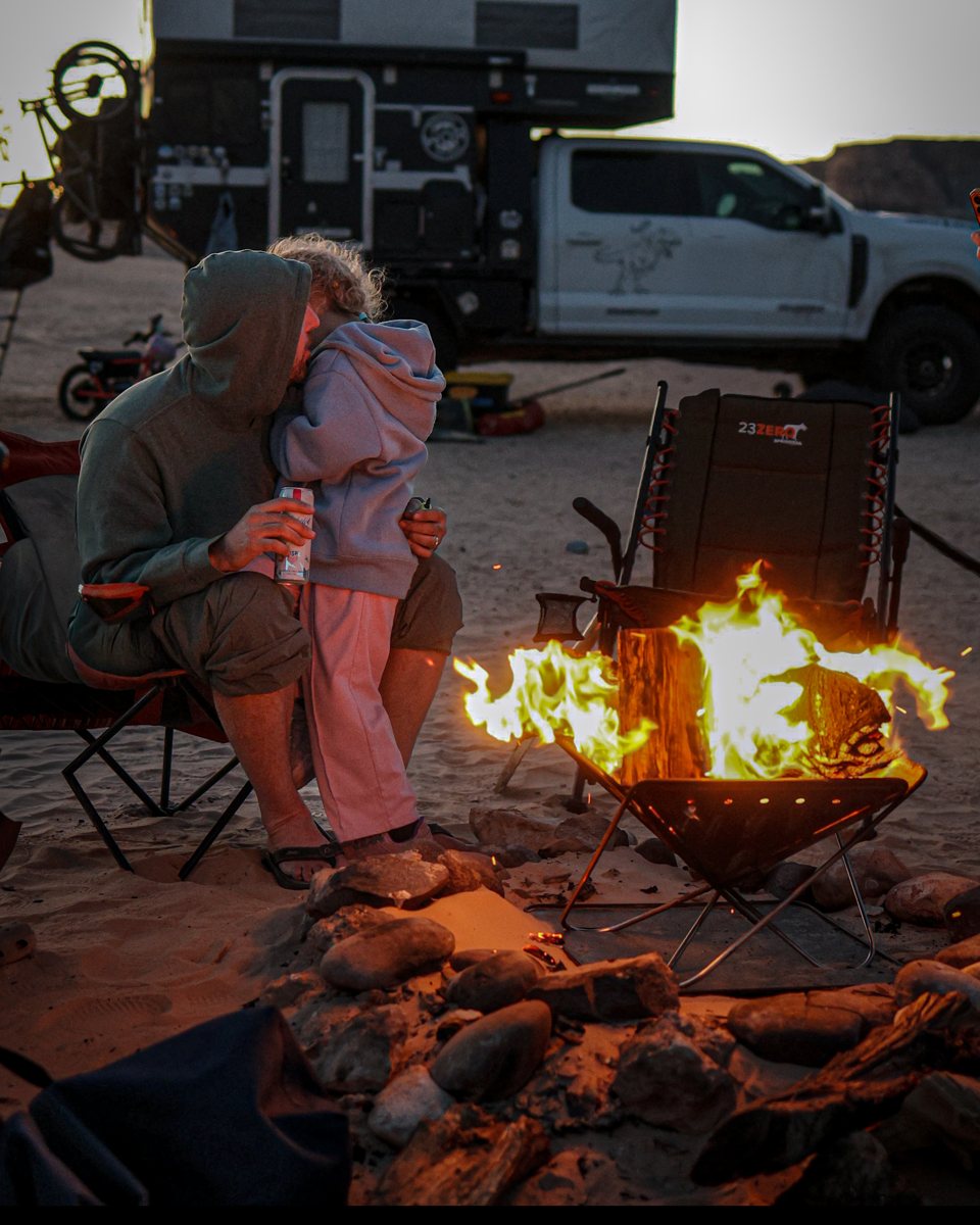 Sandy Cats founder at a desert campfire with one of his kids, the family F-250 and camper behind them